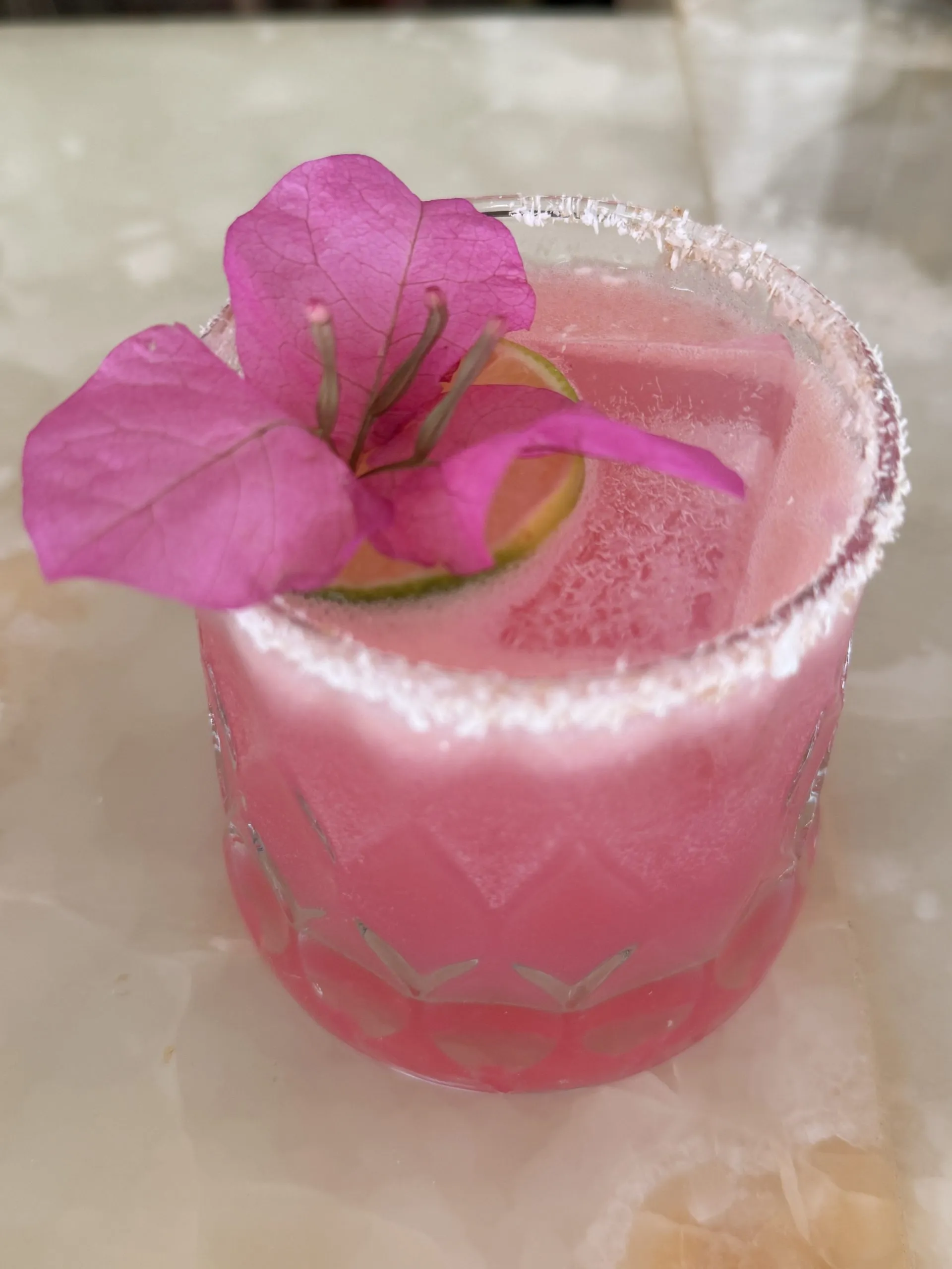 Begonvil Mezcal Margarita: tuz kenarlı pembe kokteyl, üstünde bir begonvil çiçeği.