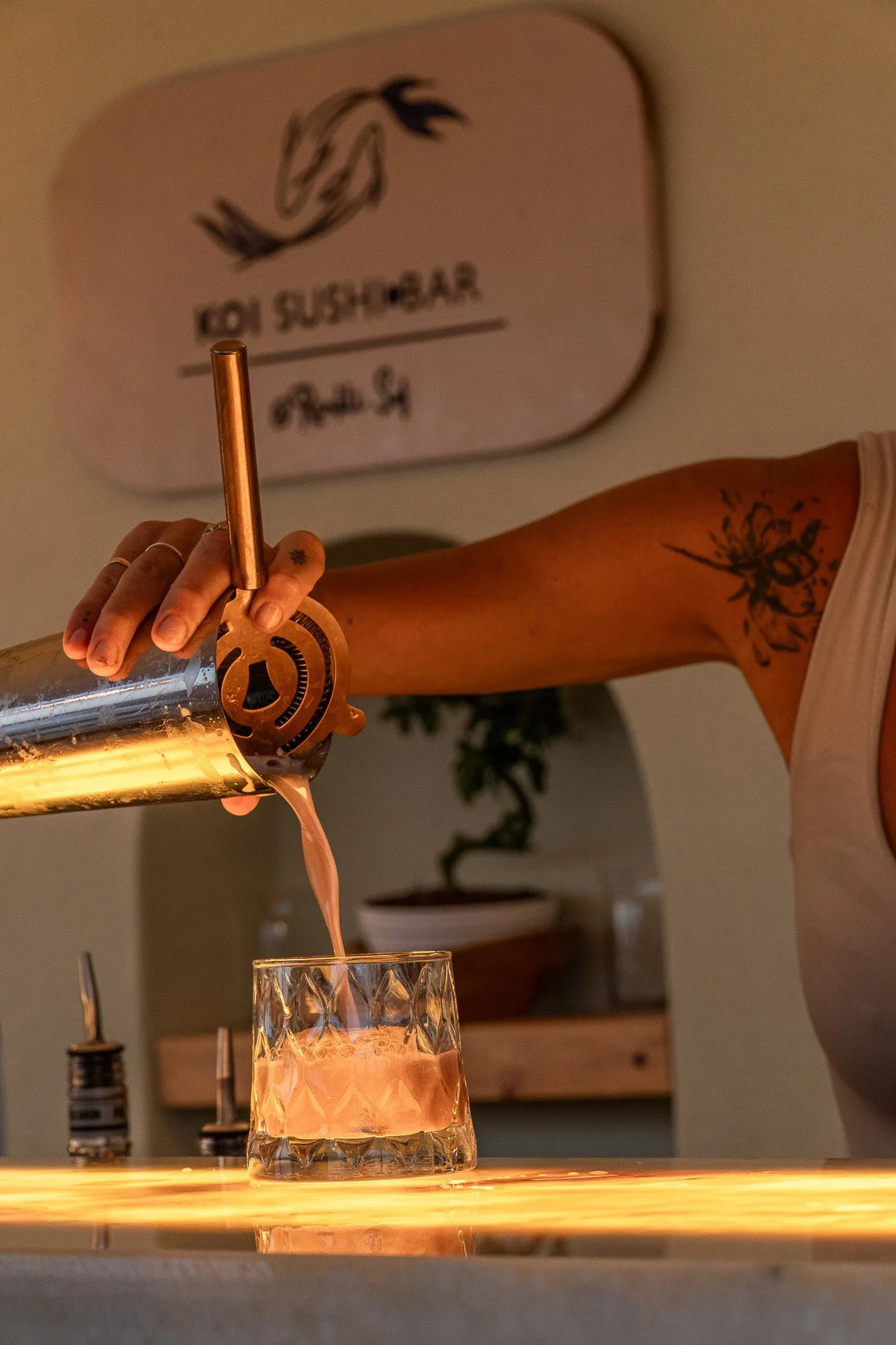 Barda, Koi Sushi Bar tabelasının önünde pembe bir kokteyl süzgeçten kesme cam bardağa dökülüyor.
